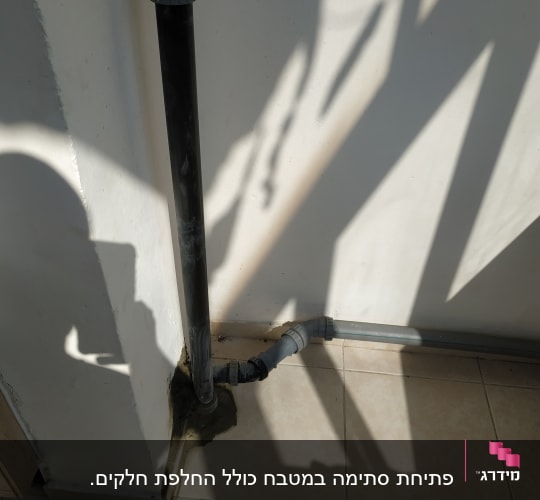 צינור ביוב שחור עם חיבורים על קיר לבן